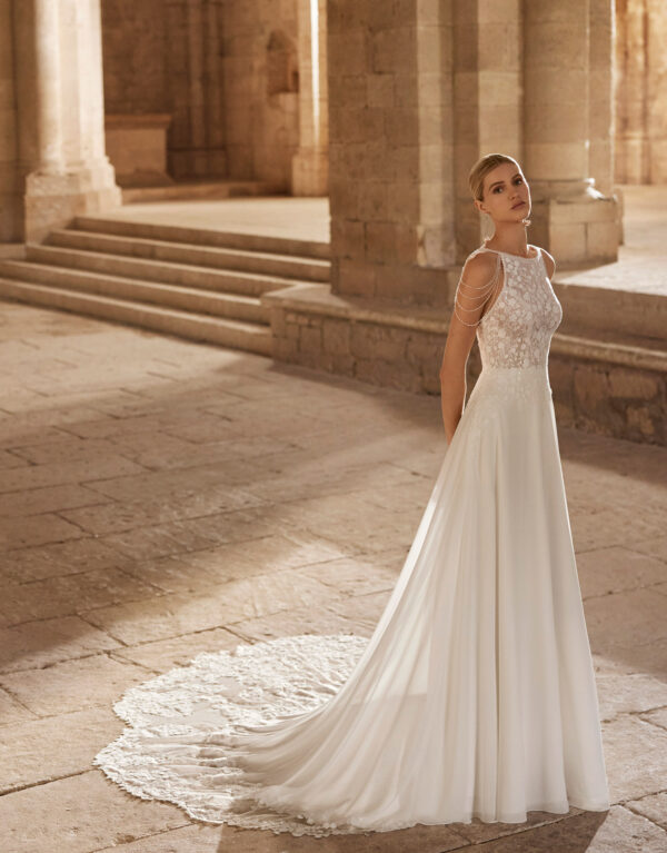 Νυφικό φόρεμα από πολύ λεπτή ανάλαφρη georgette, σε Α-line γραμμή από την νυφική συλλογή Rosa Clara. Δαντελένιο μπούστο, κεντημένο με χαντράκι με λάμψη, κλειστό μπροστά στο μπούστο λαιμόκοψη bateau και τιράντες φτιαγμένες από χάντρες σε όλη την ανοιχτή πλάτη. Ένα μοναδικό νυφικό φόρεμα από την Rosa Clará για νύφες ξεχωριστές.